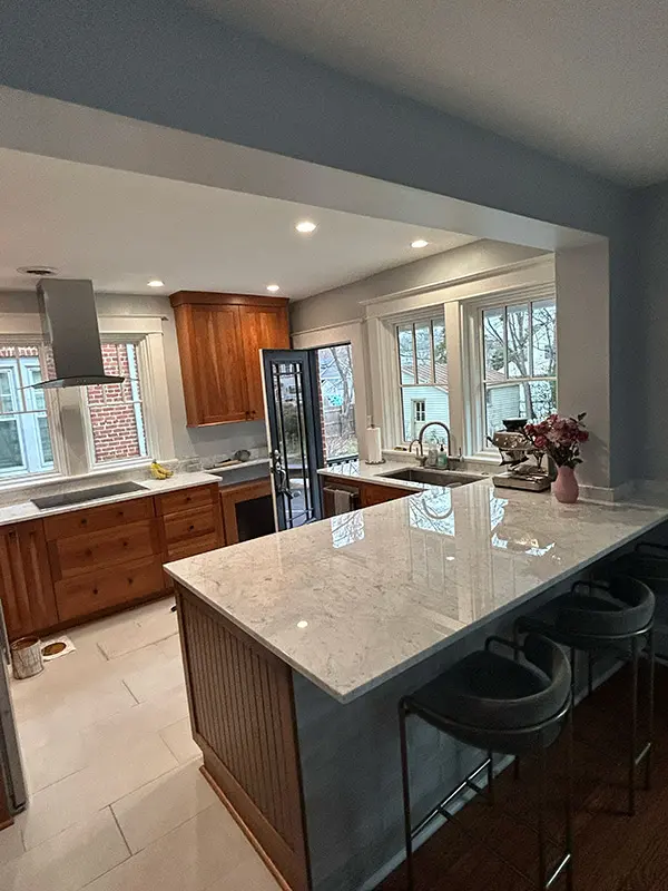 An interior kitchen scene looking towards a counter with a marble countertop, an undermount sink, and wood cabinets, next to a door leading outside to a porch.