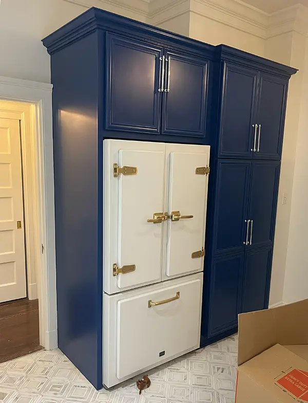 Custom tall navy-blue kitchen cabinetry framing a vintage-style white refrigerator with gold hardware.